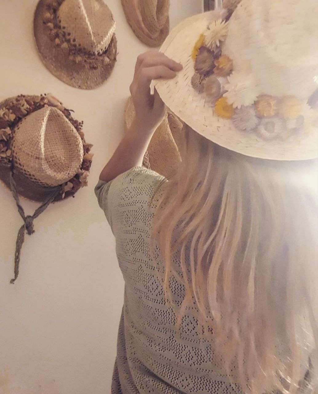 Olga triant un barret blanc amb flors seques d'una paret plena de barrets decorats